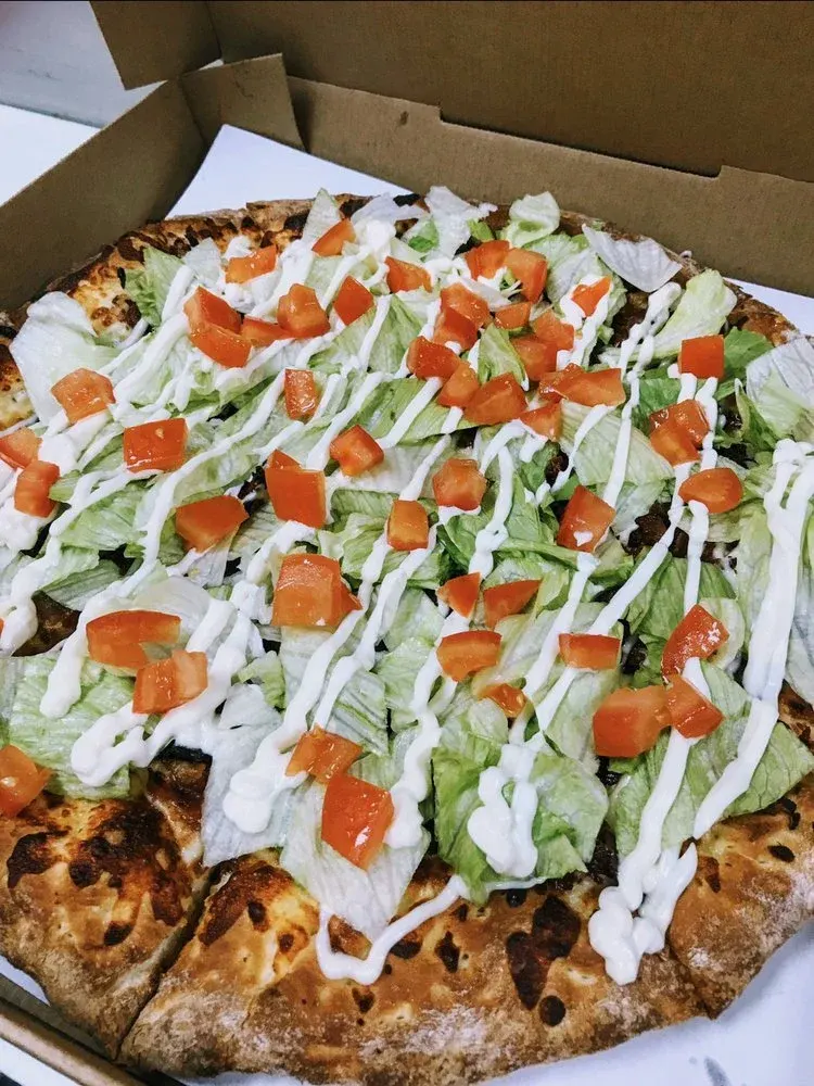 Slice of pizza topped with lettuce, chopped tomatoes, drizzled mayonnaise or ranch, and a cheese or beef crust in a pizza box.