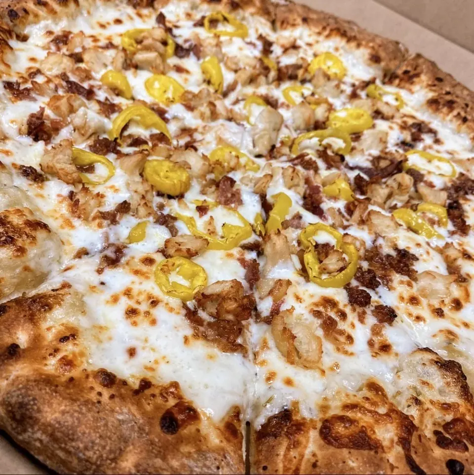 Close-up of a pizza with a golden-brown crust, topped with cheese, yellow bell peppers, and cooked chicken pieces.